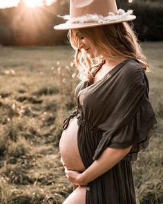 a pregnant woman wearing a hat standing in a field