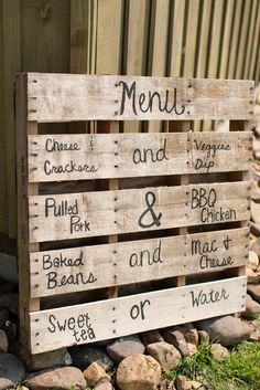 a wooden sign sitting on top of a pile of rocks next to a building with the words menu and prices written on it