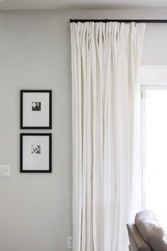 two framed pictures hang on the wall next to a window with white drapes in front of it