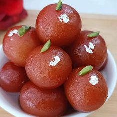 a white bowl filled with red fruit sitting on top of a wooden table next to a flower