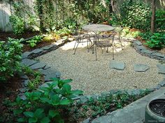 an outdoor patio with tables and chairs surrounded by greenery, rocks and gravel in the foreground