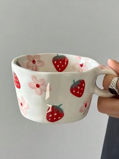 a hand holding a white cup with strawberries on it and flowers all over it