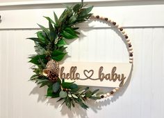 a wooden sign that says hello baby hanging on the wall next to a wreath with leaves