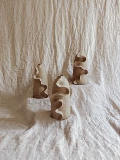 three ceramic vases sitting on top of a white cloth covered bed spread in front of them