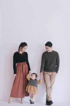 a man and woman holding hands while standing next to a small child in front of a white wall