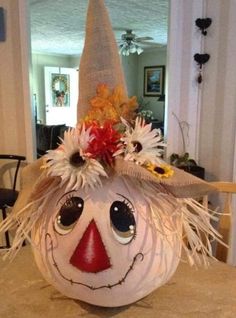 a pumpkin with a scarecrow's hat and flowers on it sitting on a table