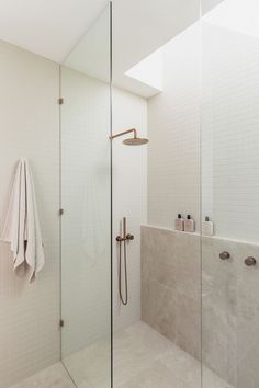 a walk in shower sitting next to a white tiled wall and counter top under a skylight