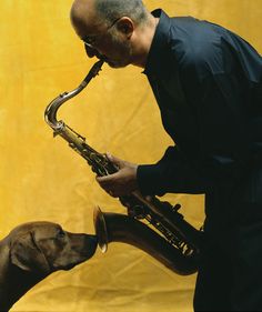 a man is playing the saxophone while his dog sniffs him out with its mouth