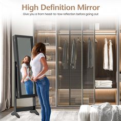 a woman standing in front of a mirror next to a walk - in closet with clothes on hangers