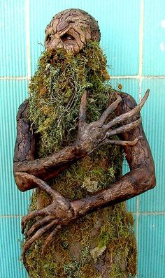 a statue of a man with moss on his face and hands in front of a blue wall