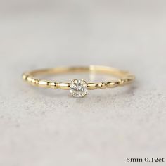 a yellow gold ring with a single diamond on the top, sitting on a white surface