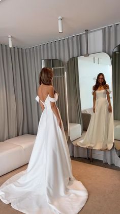 a woman in a white wedding dress looking at herself in the mirror with her back to the camera