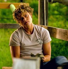 a young man sitting on a bench in front of a wooden fence and green grass