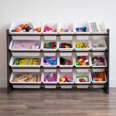 a shelf with bins filled with toys on top of wooden floor next to wall