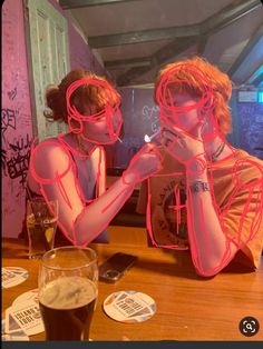 two people sitting at a table in front of a mirror with neon lights on them