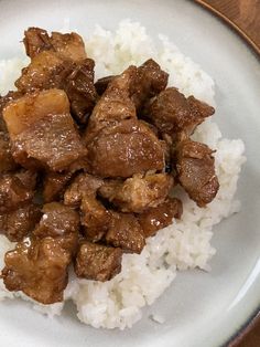 a white plate topped with meat and rice next to chopsticks on a table