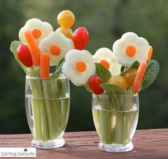 two glass vases filled with vegetables and veggies on top of a wooden table