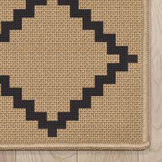 a cross stitch rug with black squares in the center on a wooden floor next to a wall