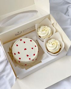 two cupcakes with white frosting and red hearts on them in a box