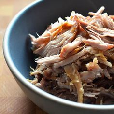 a blue bowl filled with shredded meat on top of a wooden table next to a knife