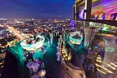 the rooftop bar is lit up at night with colorful lights on it and people sitting around