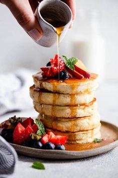 a stack of pancakes with syrup being drizzled over them and topped with berries