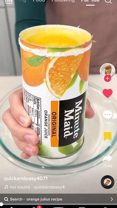 a person holding up a cup of orange juice on a glass plate with an instagram button