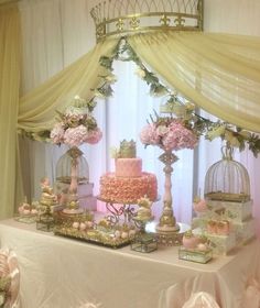 a table topped with lots of pink and white cakes next to a window covered in sheer curtains