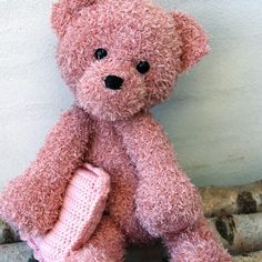 a pink teddy bear sitting on top of a pile of logs next to a wall