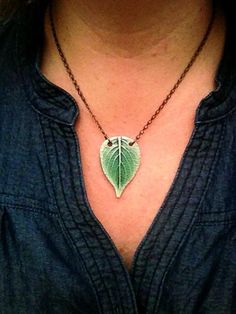 a woman wearing a necklace with a green leaf on it