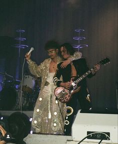 two people standing on stage with guitars and microphones in their hands, one person holding a guitar