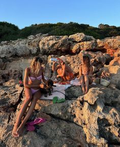 three women in bikinis sitting on rocks at the beach