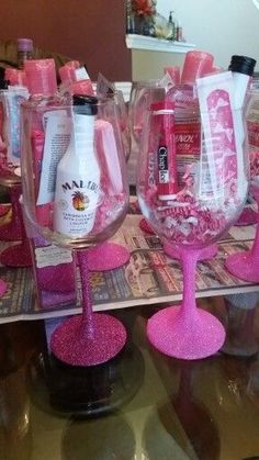 several wine glasses are lined up on a table with pink flakes and bottles in them