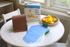 a white table topped with a bowl of yellow rubber ducks next to a book about five little ducks