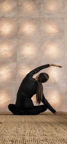 a woman sitting on the floor doing a yoga pose with her hands in the air