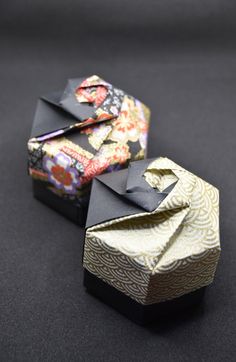 two folded boxes sitting on top of a black table next to each other, one with an origami bow at the top