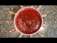 a red bowl filled with candy bars on top of a granite countertop next to a cup of sauce