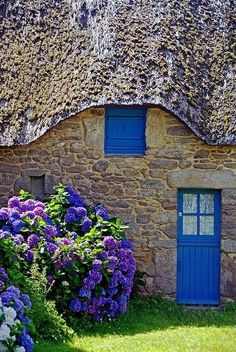 an old stone house with blue doors and flowers in the foreground, on a sunny day