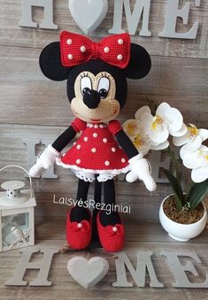 a crocheted minnie mouse doll is posed next to flowers and a sign that says home