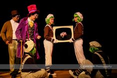 four people dressed in clown costumes holding an old tv and playing with each other on stage