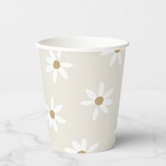 a paper cup with daisies on it sitting on a marble countertop next to a white wall