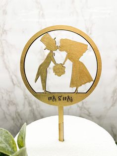 a wooden cake topper with a silhouette of two people holding hands and kissing in front of a marble background