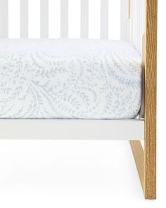 a white crib with a blue and white blanket on it's bottom half