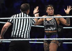 a woman standing next to a referee on top of a wrestling ring with her hands in the air