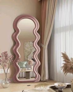 a pink mirror sitting on top of a wooden table next to a vase and flowers