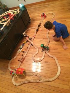 a young boy playing with a toy train set on the floor in front of a dresser