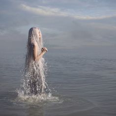 a woman standing in the water with her head covered by white hair and wearing a veil