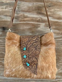 a brown and tan purse with turquoise stones on it's side sitting on a wooden surface