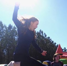 a woman jumping in the air on top of a bouncy park with other people