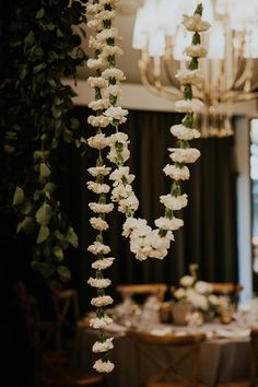 the table is set with white flowers and greenery hanging from the chandelier